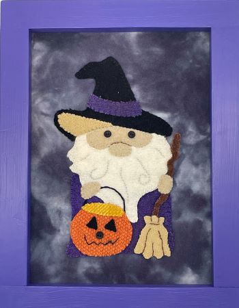 Wool applique gnome dressed as a witch and holding a jack-o-lantern and a broom.
