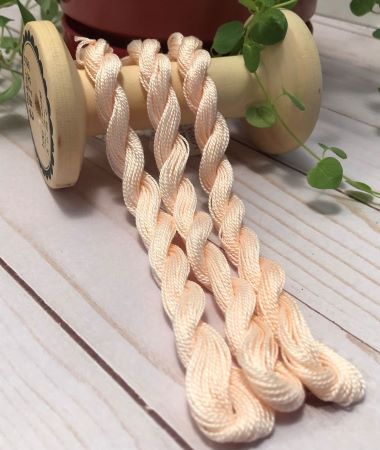 Skeins of hand dyed #8 pearl cotton in a soft peach color draped over a vintage wooden spool.