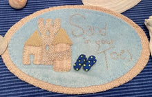 Load image into Gallery viewer, Our finished wool applique kit with a tan backing, blue background, tan sand castle, flip flop buttons and letters embroidered with a variegated tan pearl cotton.
