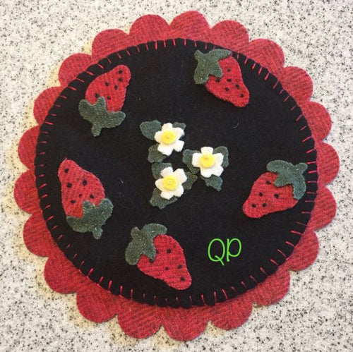 Wool applique 6 inch mat with four  strawberries on a black, round circle mat on a slightly larger, red, scallloped mat
