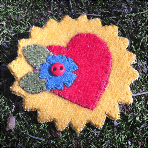 Sunshine Of My Heart Laser Cut Wool Pin Kit has a round sun with a red heart, blue flower and green leaves on it.