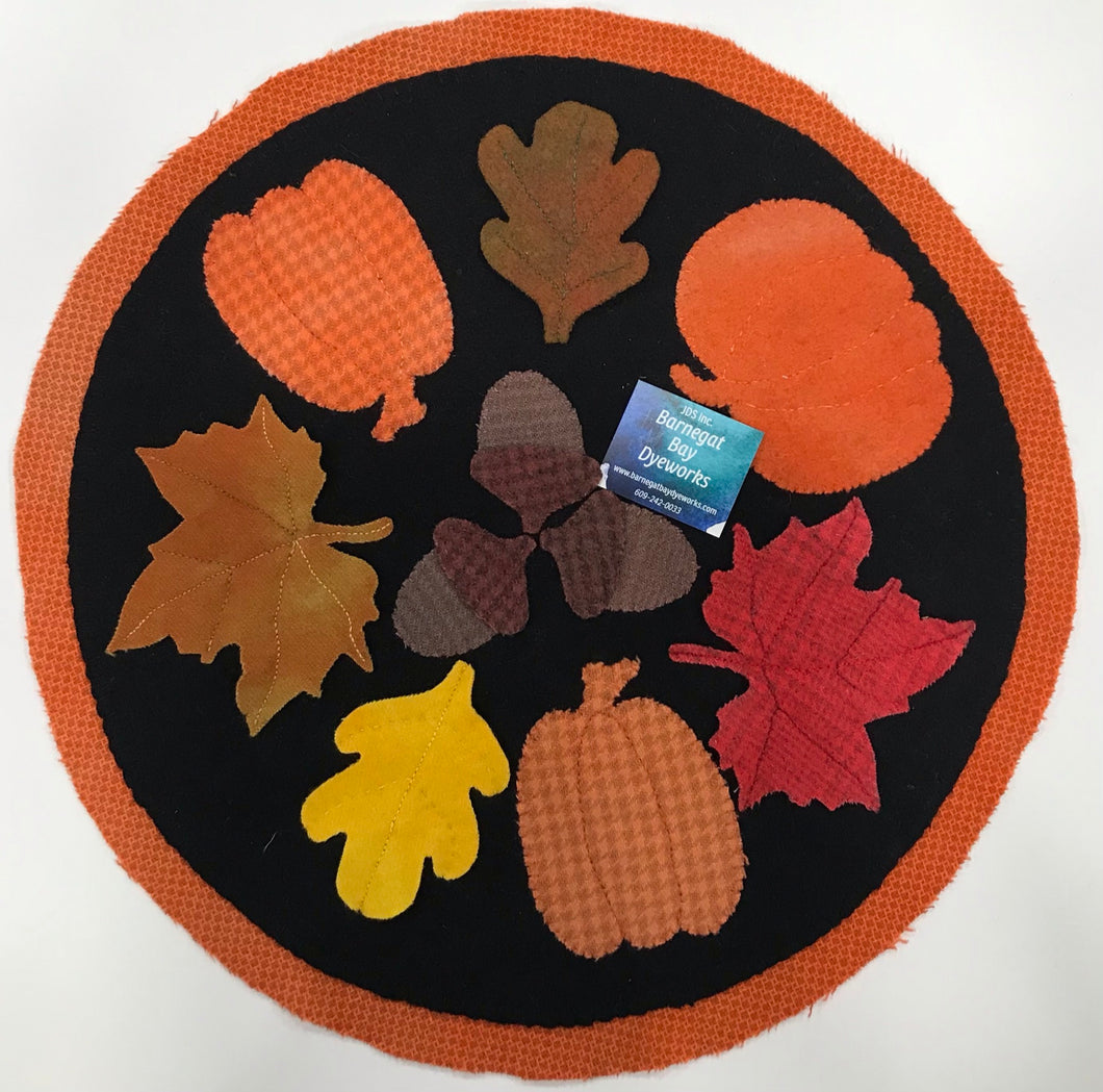 Fall round table topper in wool applique with colorful pumpkins, leaves and acorns stitched in the center of a black background with a orange backing forming the  border.