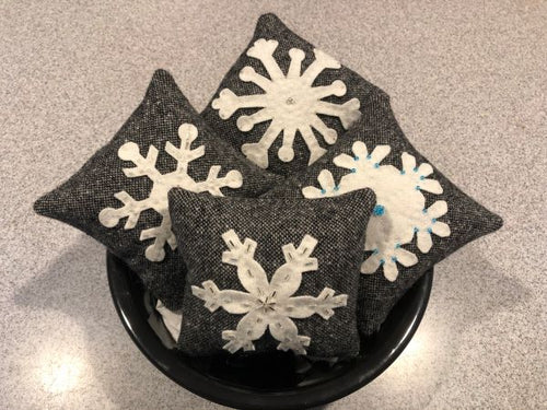 Four wool applique bowl stuffers with die cut, white, wool snowflakes on a black with white speckled flannel in a black bowl