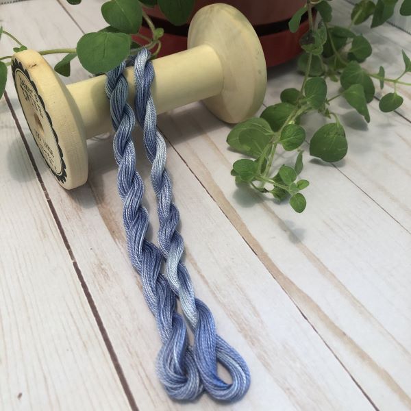 Hand dyed #12 pearl cotton threads in﻿﻿ variegated light to dark blue draped over a vintage thread spool.
