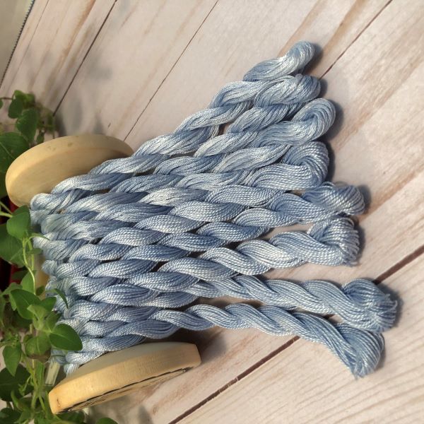 Hand dyed floss & pearl cotton threads in﻿﻿ variegated medium blues draped over a vintage thread spool.