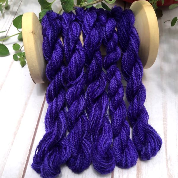 Skeins of hand dyed wool thread in a rich, dark purple slightly variegated.