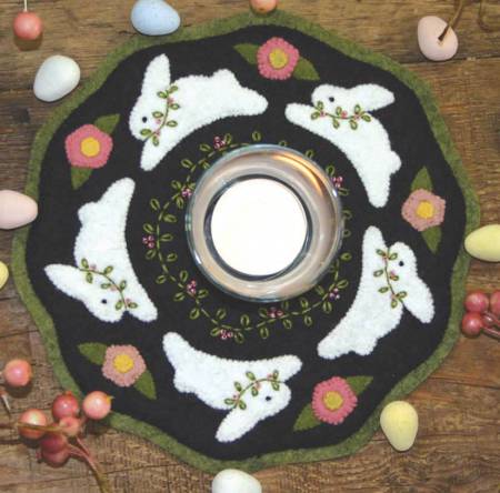 A wool scalloped mat with applique bunnies and flowers with an hand embroidery floral vine around the center.  