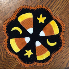 Load image into Gallery viewer, Wool applique scalloped round mat of four large candy corns separated by smaller stars and quarter moons on a black background all on a larger orange wool mat.  Brightly colored wools.
