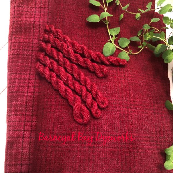 Two pieces of a hand dyed textures in a medium dark red with skeins of wool thread. Wool and thread dyed together to match