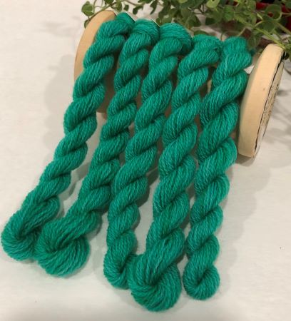 Skeins of hand dyed wool thread in Caribbean Green is a midtone, subdued, emerald aqua-green with a hint of blue undertone