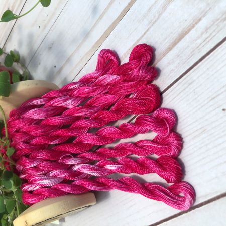 Eight skeins of hand dyed, variegated, pinkish red threads draped over a vintage thread spool.