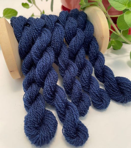 Five skeins of wool thread in a medium dark blue with slight variations, draped over a vintage thread spool.