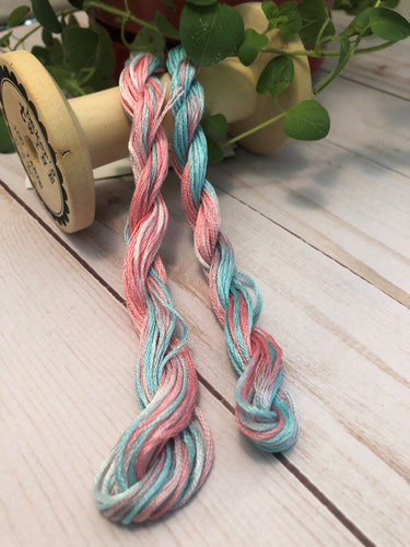 Hand dyed, 6 strand floss in cotton candy colors of pink and blue draped over a vintage thread spool