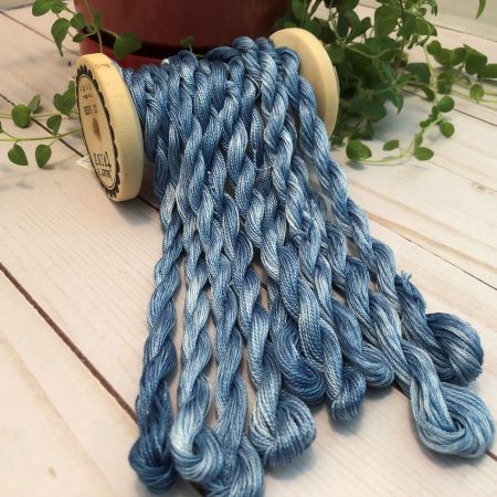 Twisted skeins of hand dyed threads in denim blue draped over a vintage thread spool.