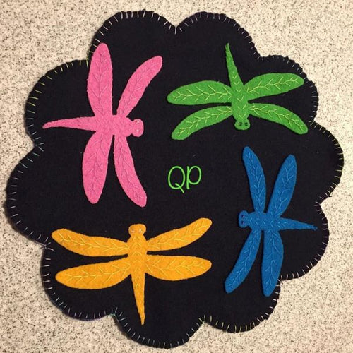 Colorful die cut dragonflies in bright green, pink, yellow and blue on a die cut navy scalloped wool mat.