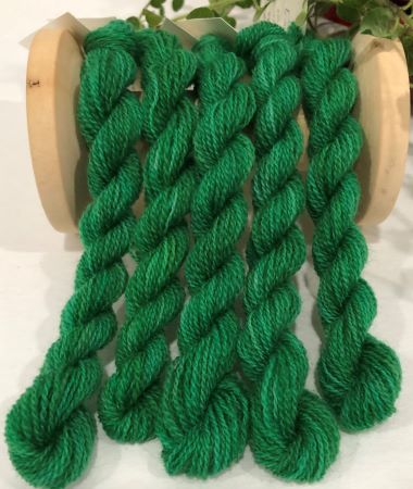 Skeins of hand dyed wool thread in a variegated, medium dark green with a hint of blue.