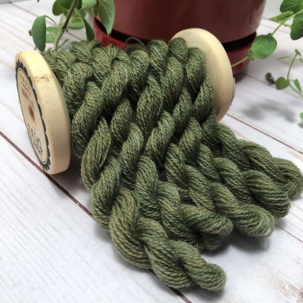 Six skeins of wool thread in a color that reminds me of geranium leaves, draped over a vintage thread spool.
