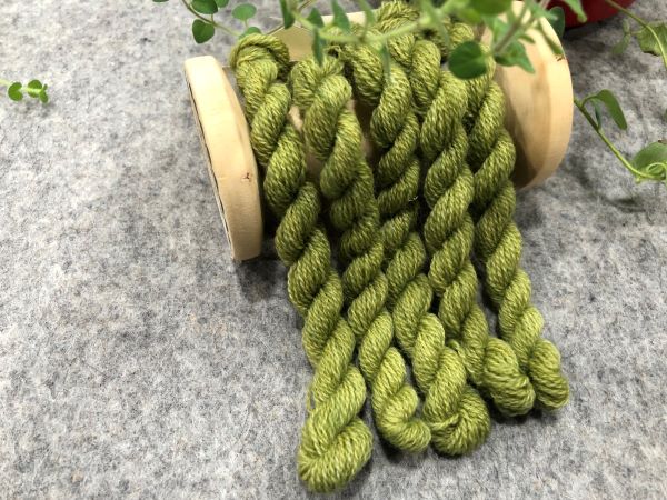 Hand dyed wool thread in a medium green draped over a vintage spool.