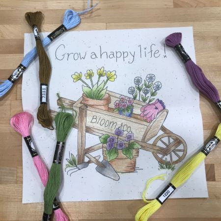 Grow A Happy Life Embroidery Pattern of a wooden wheel barrow with flowering plants, garden tools, gloves and the works 