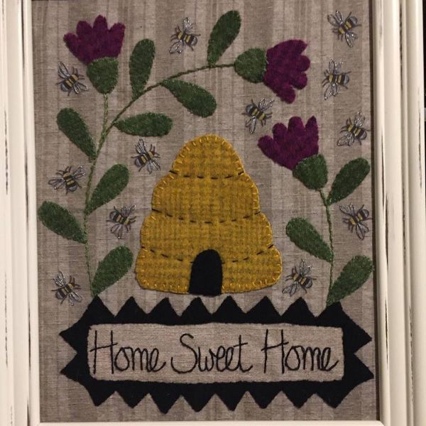 Home Sweet Home (Bees) Wool Kit designed by All Through The Night Designs on a cotton background with bees, wool applique purple flowers, green leaves, a yellow bee skep and a banner that says 