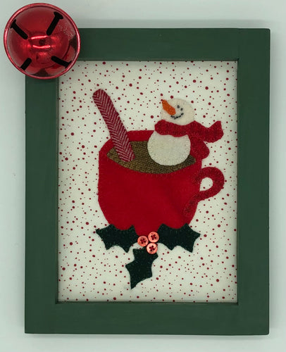 Wool applique kit of a marshmallow snowman floating in a mug of cocoa with a peppermint stick.  Three holly leaves and berries are at the base of the cup.