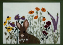 Load image into Gallery viewer, Wool applique scene of a brown rabbit in a field of flowers eating clover.  This pieces uses hand dyed wool for applique, hand embroidery and a hand dyed cotton background.
