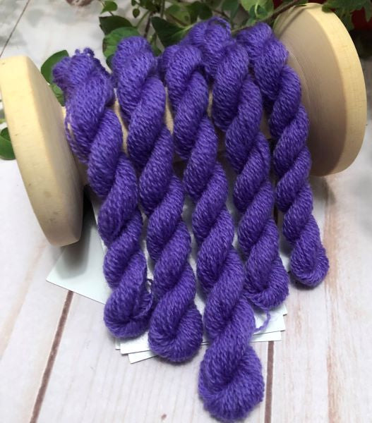 Five skeins of a light medium purple hand dyed wool thread draped over a vintage thread spool.