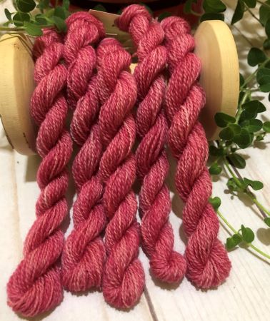 Five skeins of hand dyed, variegated wool thread in soft vintage, light to medium dark pinks. draped over a vintage spool.