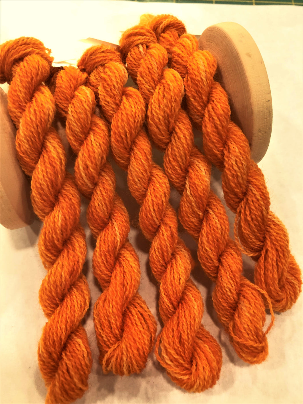 Hand dyed wool thread in a variegated oranges from yelllowish orange to a medium orange.