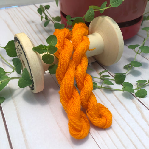 Skeins of hand dyed wool thread in a bright , medium orange.