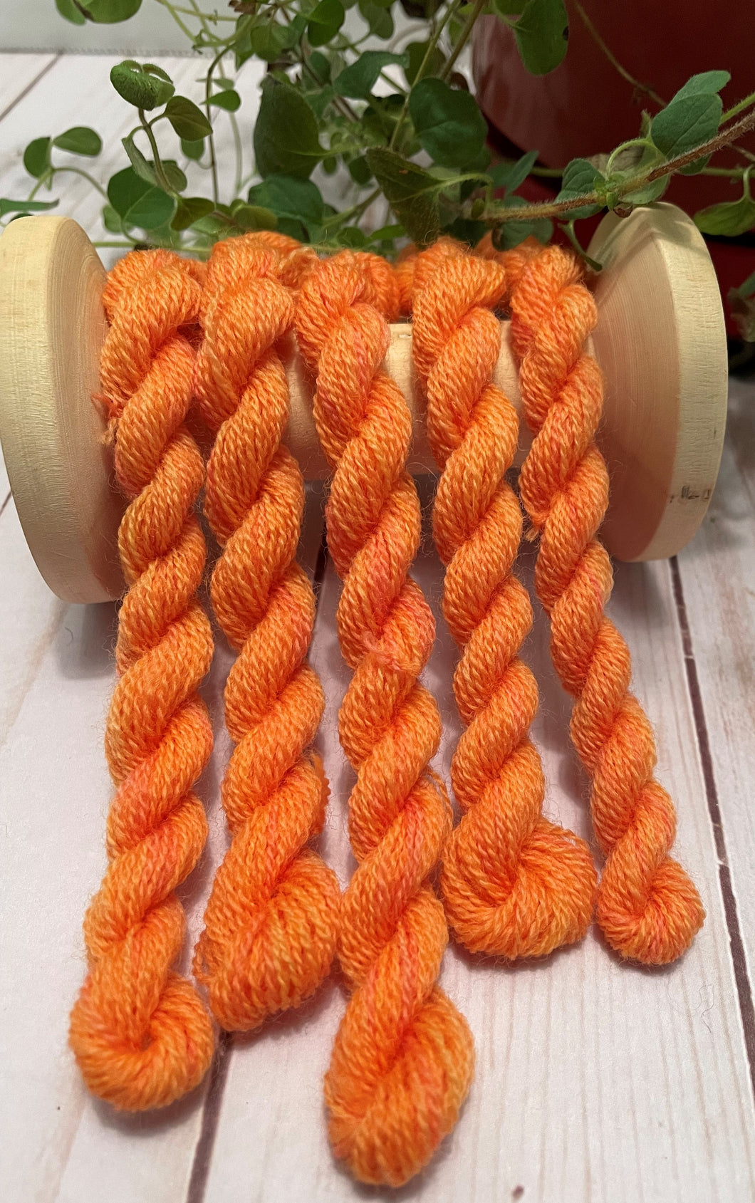 Skeins of hand dyed, medium orange wool thread with yellow and reddish highlights.