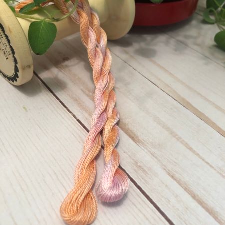 Hand Dyed #8 pearl cotton skeins in soft orange and pink draped over a vintage spool.