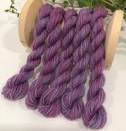 Skeins of hand dyed wool threads in a variegated purples and blues colorway.