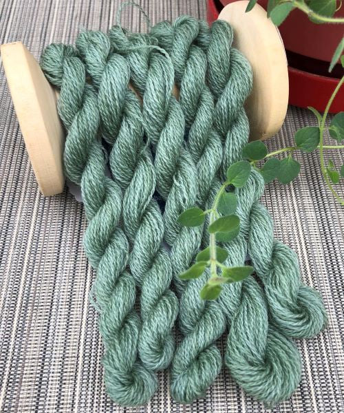 Skeins of hand dyed wool thread in sage green .
