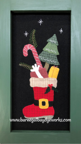 Sample made from our wool applique kit for Santa's Jolly Boot.  One red Santa boot facing left , filled with a red present with a bow, a candy cane, small evergreen tree and a yellow present.