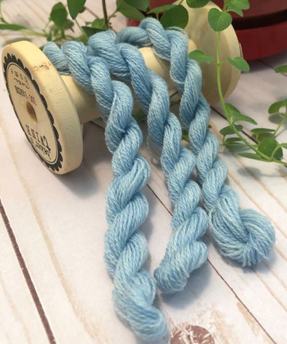 Three skeins of a light blue slightly variegated hand dyed wool thread draped over a vintage thread spool.