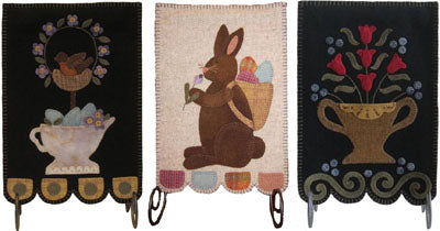 Spring Banners pattern has three projects - a robin nesting in a wreath over a pitcher filled with eggs and flowers, a rabbit with a back pack full of eggs smelling a flower and a two handled vase with red flowers.  Primitive style projects.