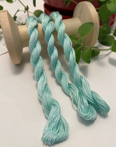 Hand dyed, teal, #8 pearl cotton threads ﻿draped over a vintage thread spool.