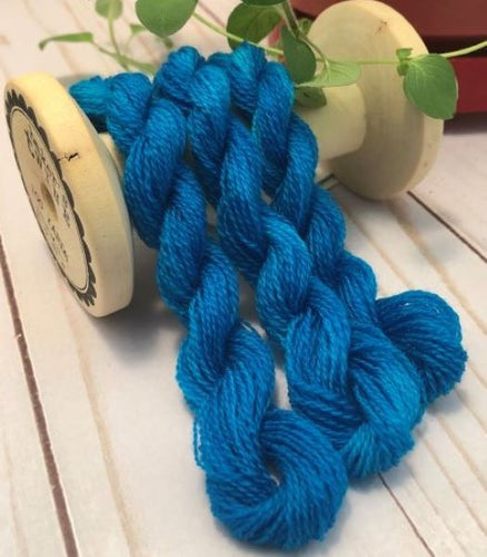 Hand dyed skeins of wool threads in﻿﻿ slightly variegated turquoise draped over a vintage thread spool.