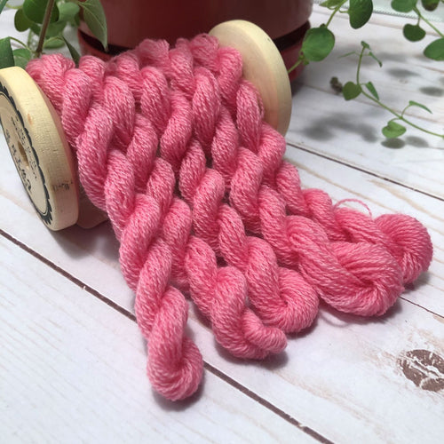 Skeins of warm, medium pink, hand dyed wool thread draped over a vintage thread spool.