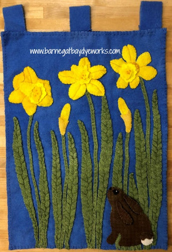 Wool applique scene of a tiny brown bunny lookin up at daffodils.