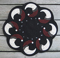 Jolly Nicks Pattern by Plays With Wool scalloped mat with eight Santa heads and hats in the shape of a quarter moon around the edge of a scalloped mat in wool applique